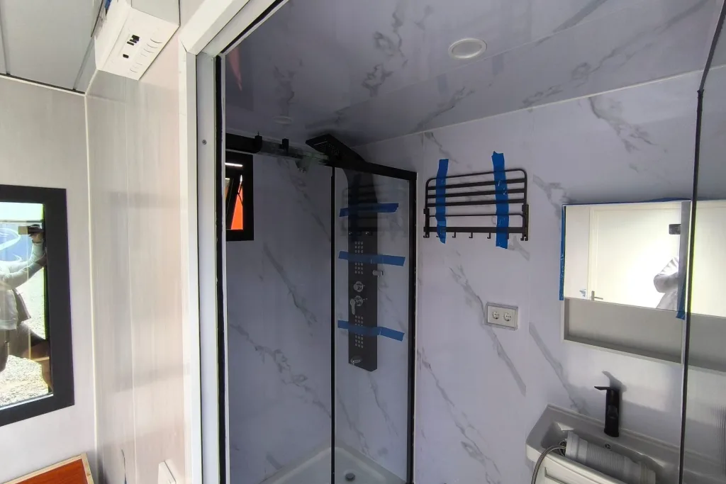 Baño con ducha de cristal de marco negro y paredes que imitan mármol